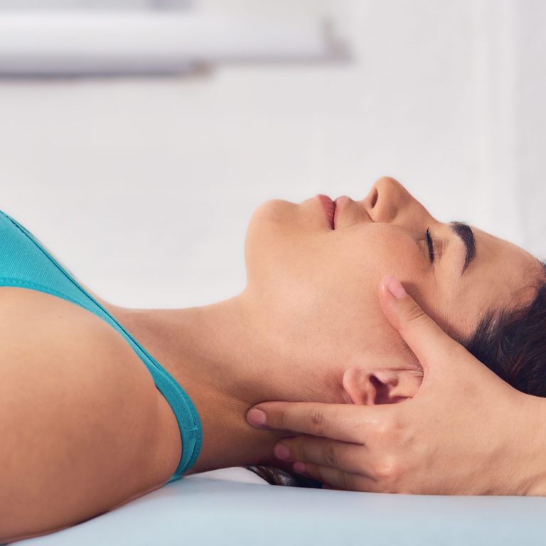 Gentle craniosacral therapy performed by an osteopath, targeting neck pain on young beautiful woman in blue top. Close up